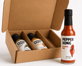 A cardboard gift box with three Pepper Song hot sauce bottles inside, alongside one Pepper Song hot sauce bottle standing outside on a white background.